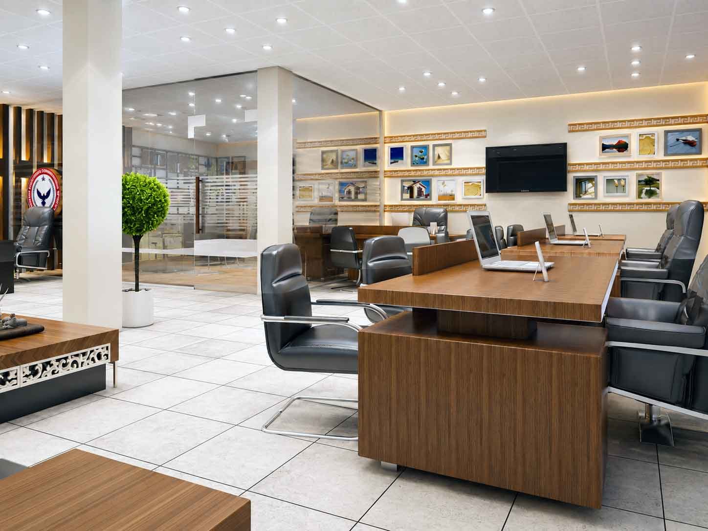 Open-plan office workstation with wooden desks, laptops, and wall-mounted TV screen