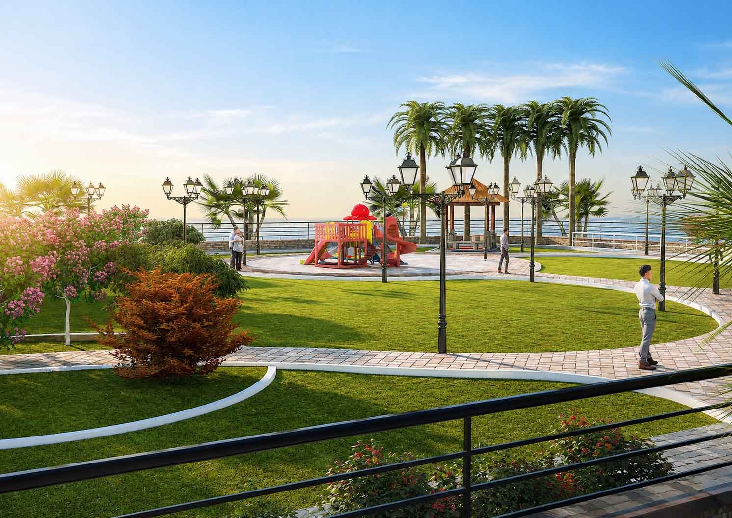 Ground-level view of a colorful children's playground surrounded by ornate lamp posts and palm trees, overlooking the sea in a waterfront park.