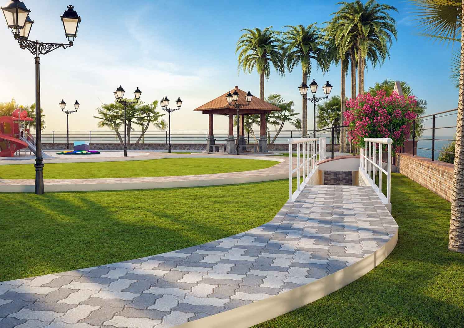 Curved paved walkway with a bridge and railing leading toward a wooden gazebo and palm trees overlooking the sea in a landscaped park.